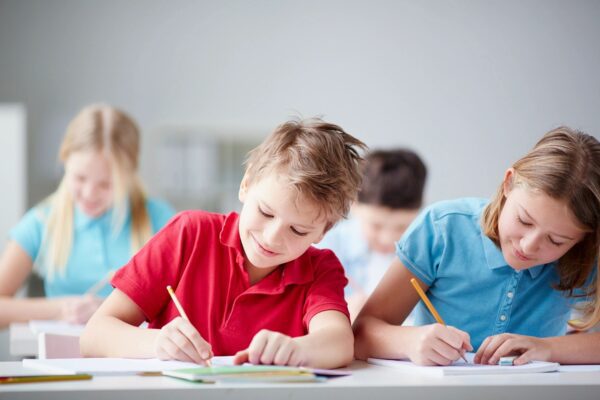 two kids writing with pencils in a notebook